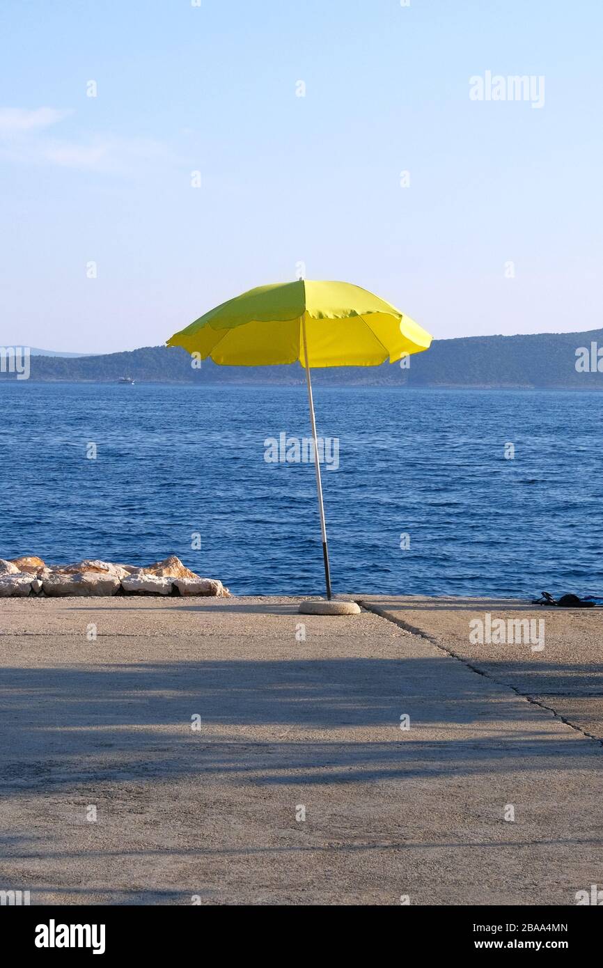 Gelber Sonnenschirm an der Sommerküste. Der Strand mit Sonnenschirm wartet bei Sonnenuntergang auf Touristen. Happy Summer Vacations Konzept. Vertikale Ansicht. Stockfoto
