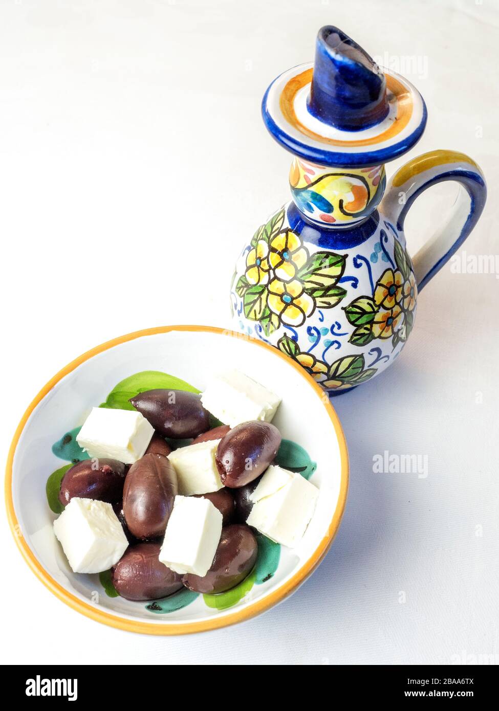 Kalamata-Oliven und Fetakäse in einer Schüssel mit dekorativer Ölkanne auf einem weißen Tischtuch Stockfoto