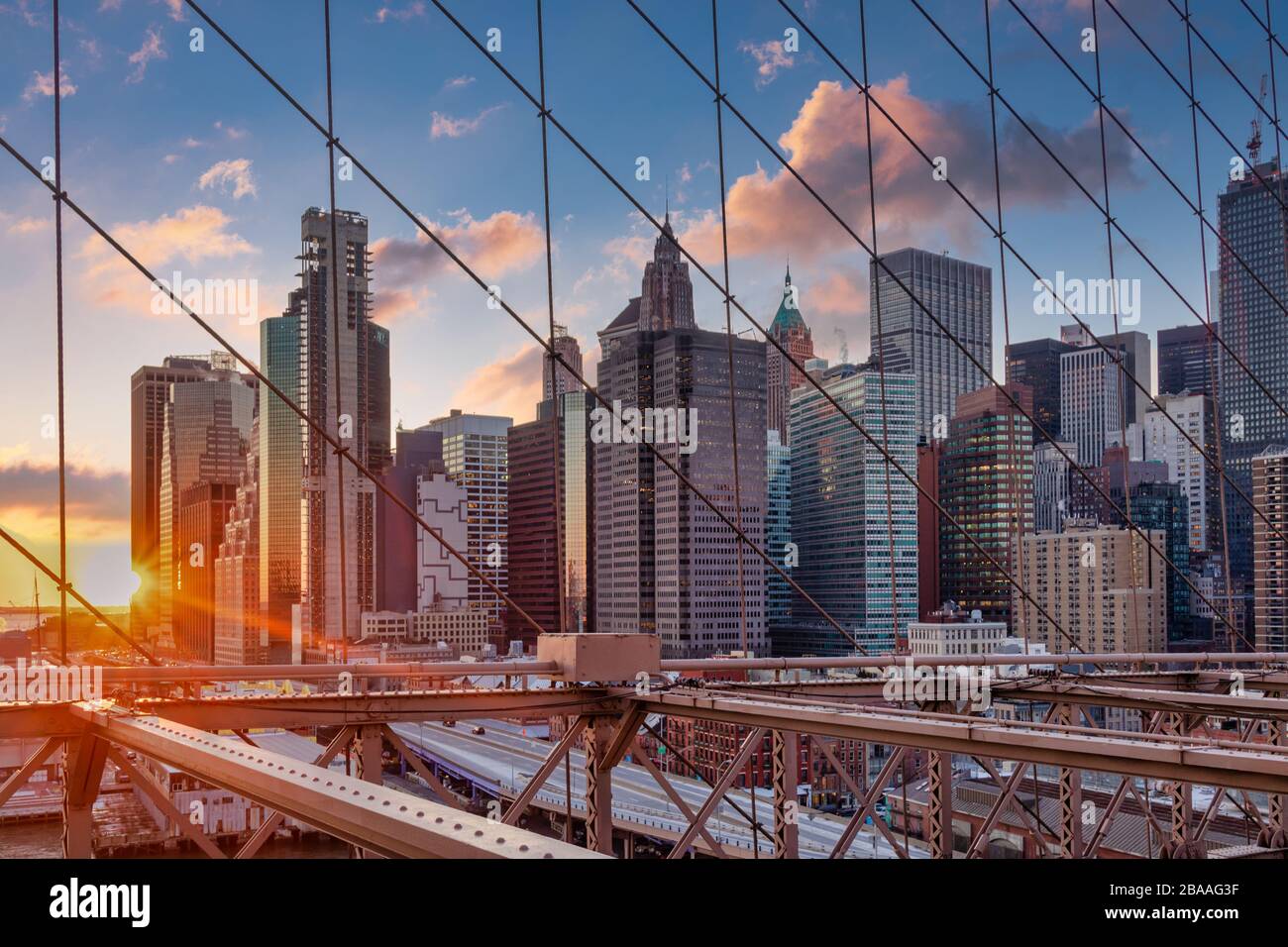 New York Skyline von Brooklyn Bridge bei Sonnenuntergang im Winter mit Wolken am Himmel im Hintergrund Stockfoto