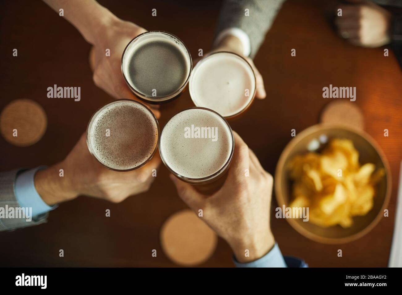 Nahaufnahme von Freunden, die mit einer Brille Bier toasten und Pommes am Holztisch essen Stockfoto