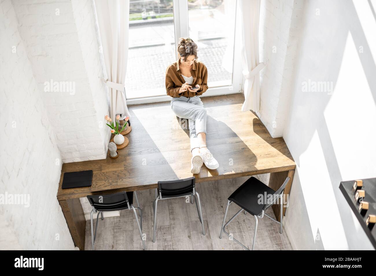 Frau sitzt mit Telefon auf der riesigen Fensterbank zu Hause, Blick von oben Stockfoto