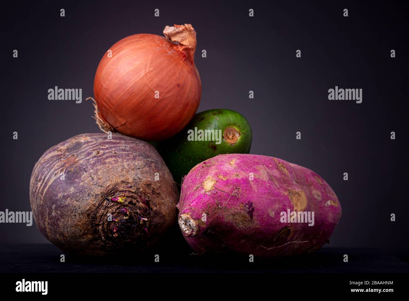 Haufen aus roten Beeten, Avocado und Rosenkartoffeln Obst und Gemüse mit einer orangefarbenen Zwiebel oben vor dunklem Hintergrund Stockfoto