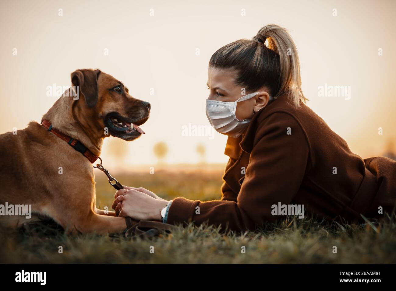 Frau, die eine Schutzmaske trägt, geht allein mit einem Hund im Freien wegen der Corona-Virus-Pandemie Kovid-19 Stockfoto