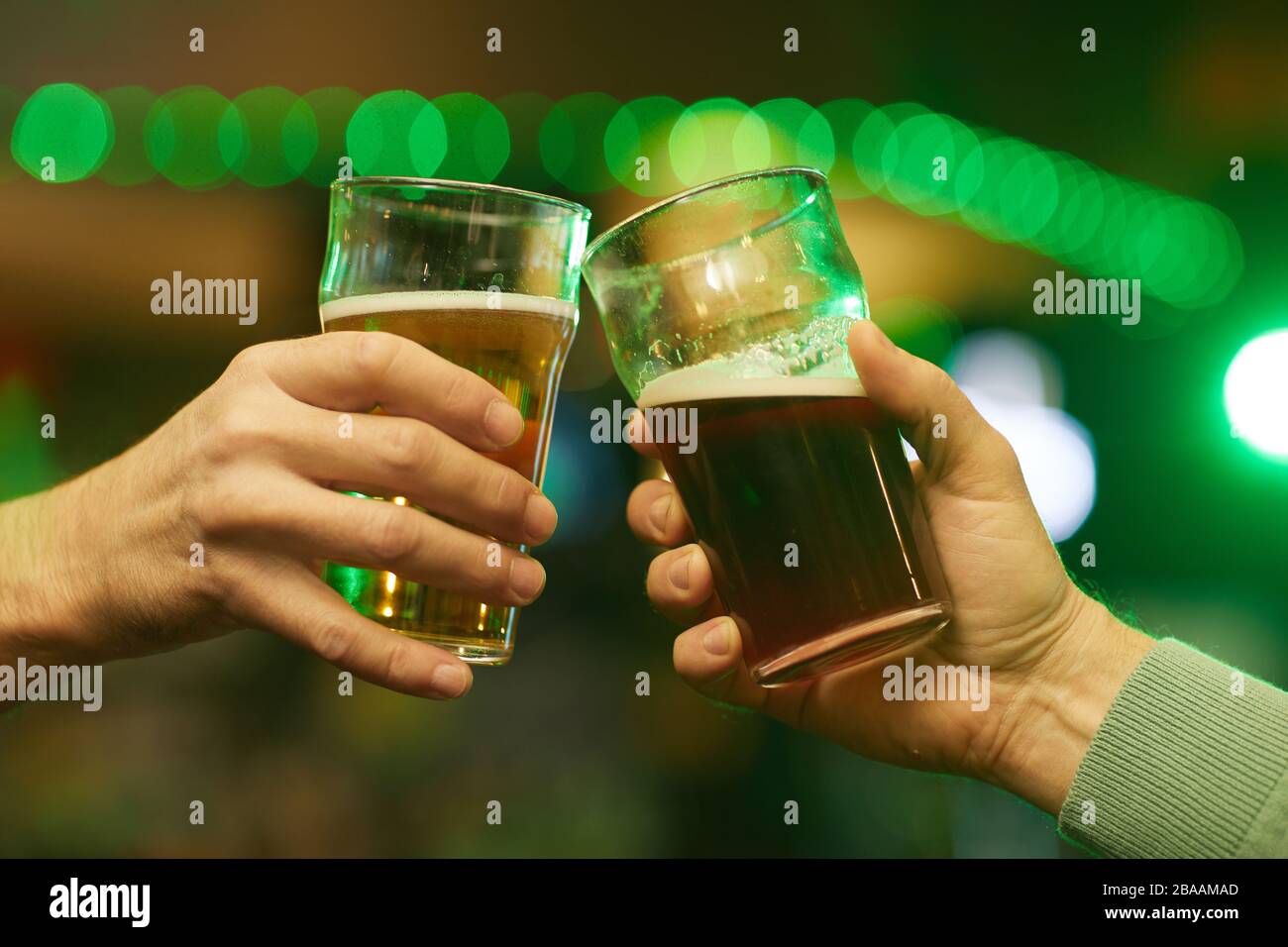 Nahaufnahme von zwei männlichen Händen, die eine Brille mit Bier und Toasten halten Stockfoto