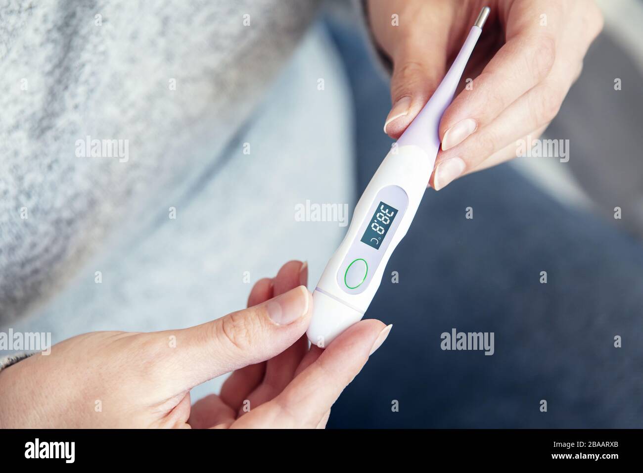 Das Handthermometer der Frau zeigt eine hohe Körpertemperatur Stockfoto