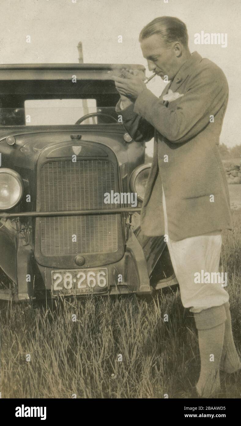 Antikfoto von 1924, ein Herr beleuchtet eine Pfeife vor seinem Auto. Genaue Lage unbekannt; das Kennzeichen stammt aus Rhode Island. QUELLE: ORIGINALFOTO Stockfoto