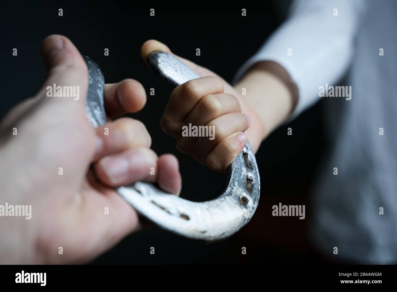 Sicht auf die kaukasische männliche Hand, die einem Kind mit weißem Hemd einen glänzenden polierten Horschuh aus Stahl in natürlichem Licht gibt Stockfoto