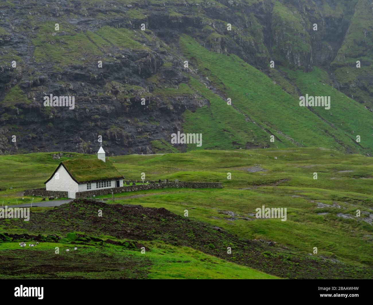 Faröer Inseln, Streymoy, Saksun. Blick auf Saksuns Kirche und das Tal. Weißes Gebäude mit Rasendach, das aus den Grünfeldern heraussteht. Stockfoto