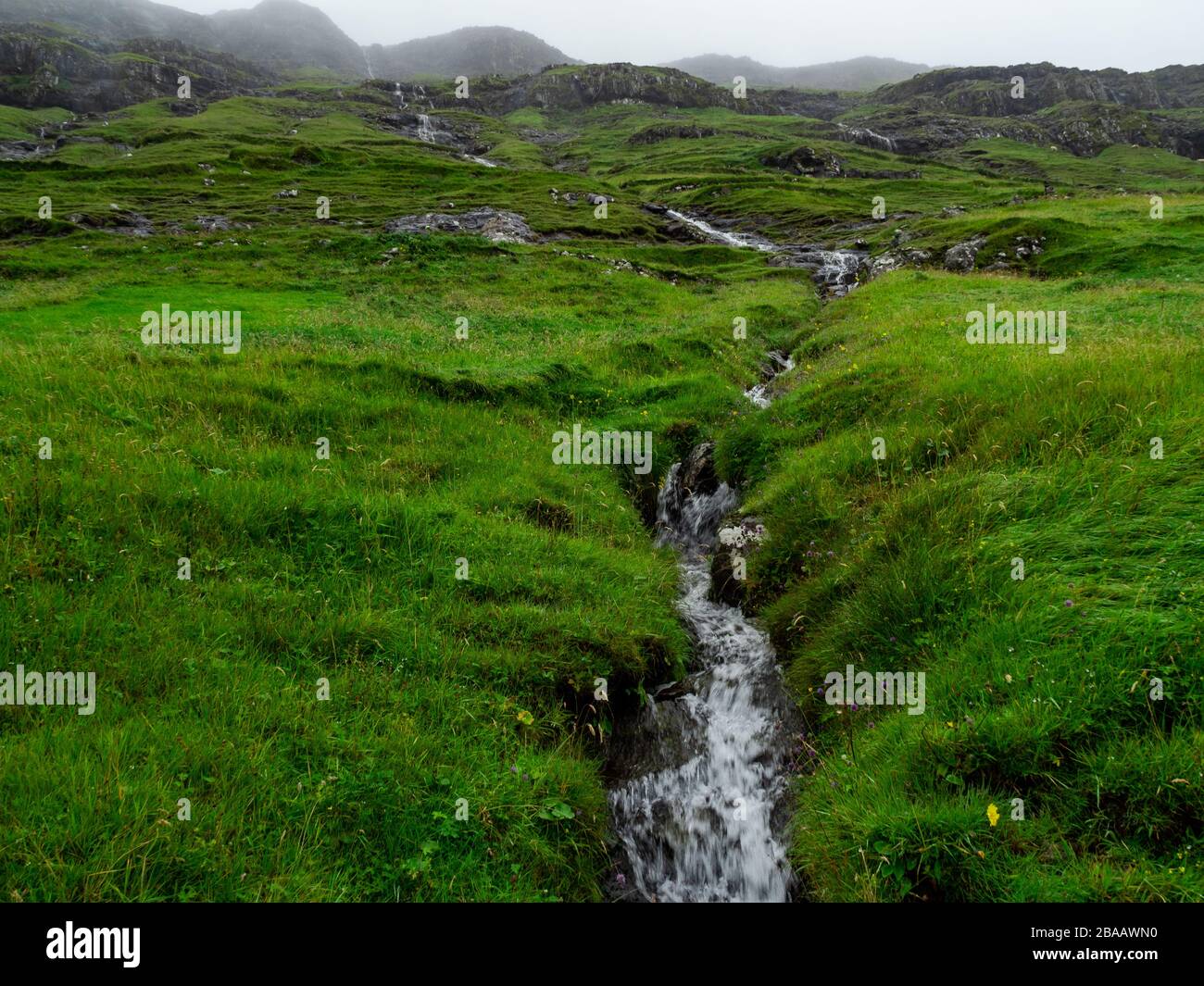 Die Färöer sind das Land der Wasserfälle, die grüne Felder durchschnitten und in den Ozean fallen. Stockfoto