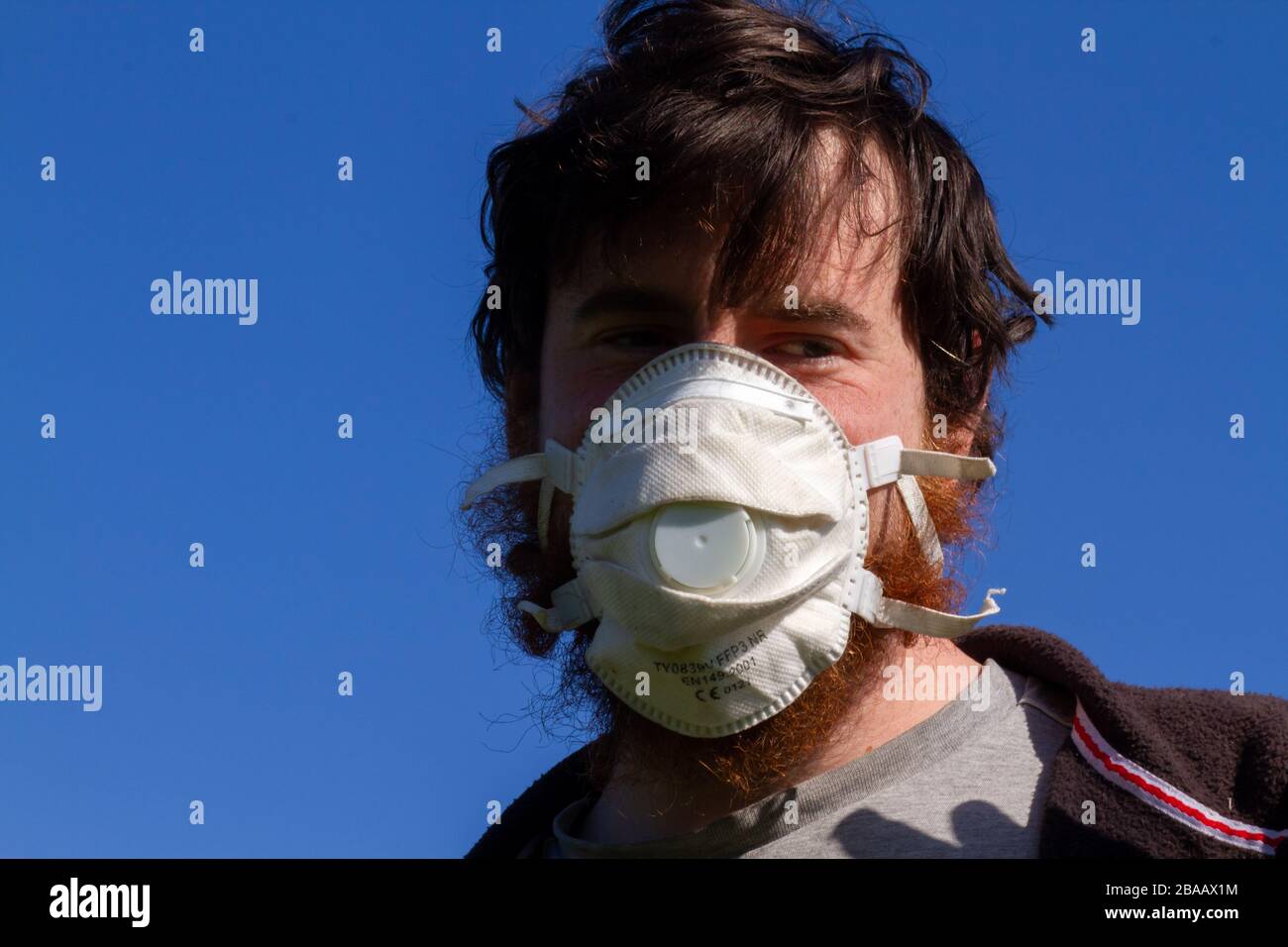 Junger kaukasischer Mann, der eine Gesichtsmaske vor einem blauen Himmel trägt Stockfoto