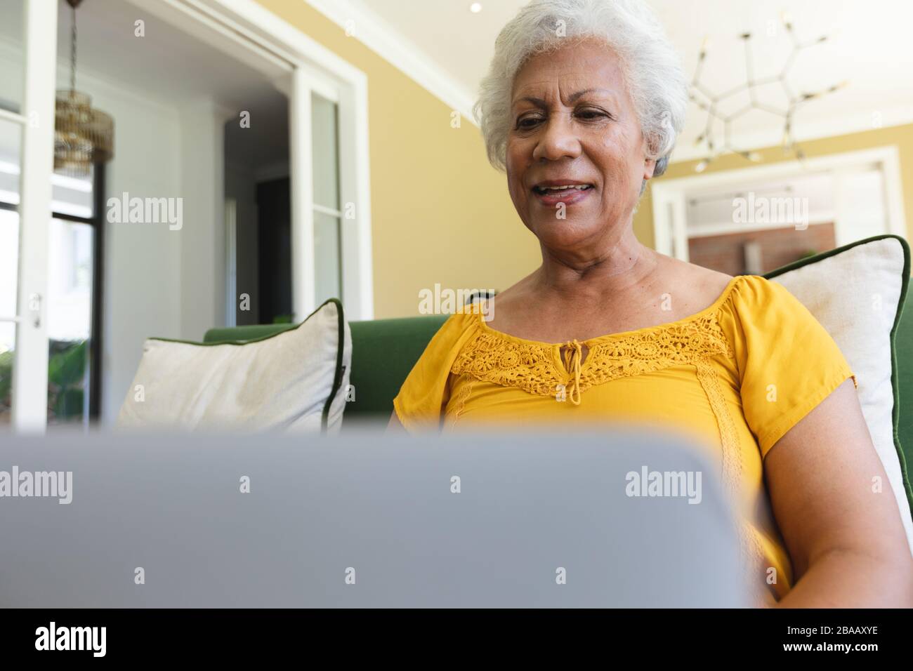 Die ältere afroamerikanische Frau, die mit einem Laptop in einer Kanape sitzt Stockfoto