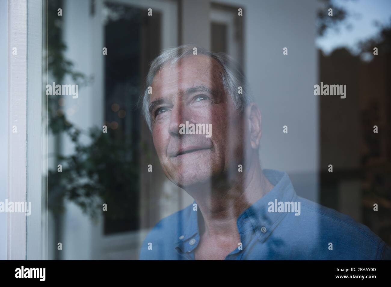 Kaukasischer Senior, der zu Hause über das Fenster blickt Stockfoto