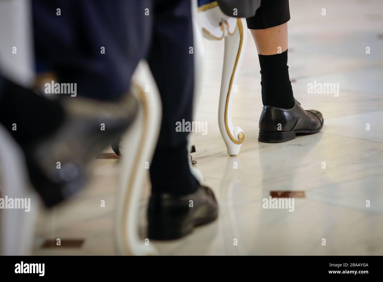 Details mit den Schuhen, Socken und Hosen eines Mannes, der auf einem Stuhl sitzt und seine Haut enthüllt. Stockfoto