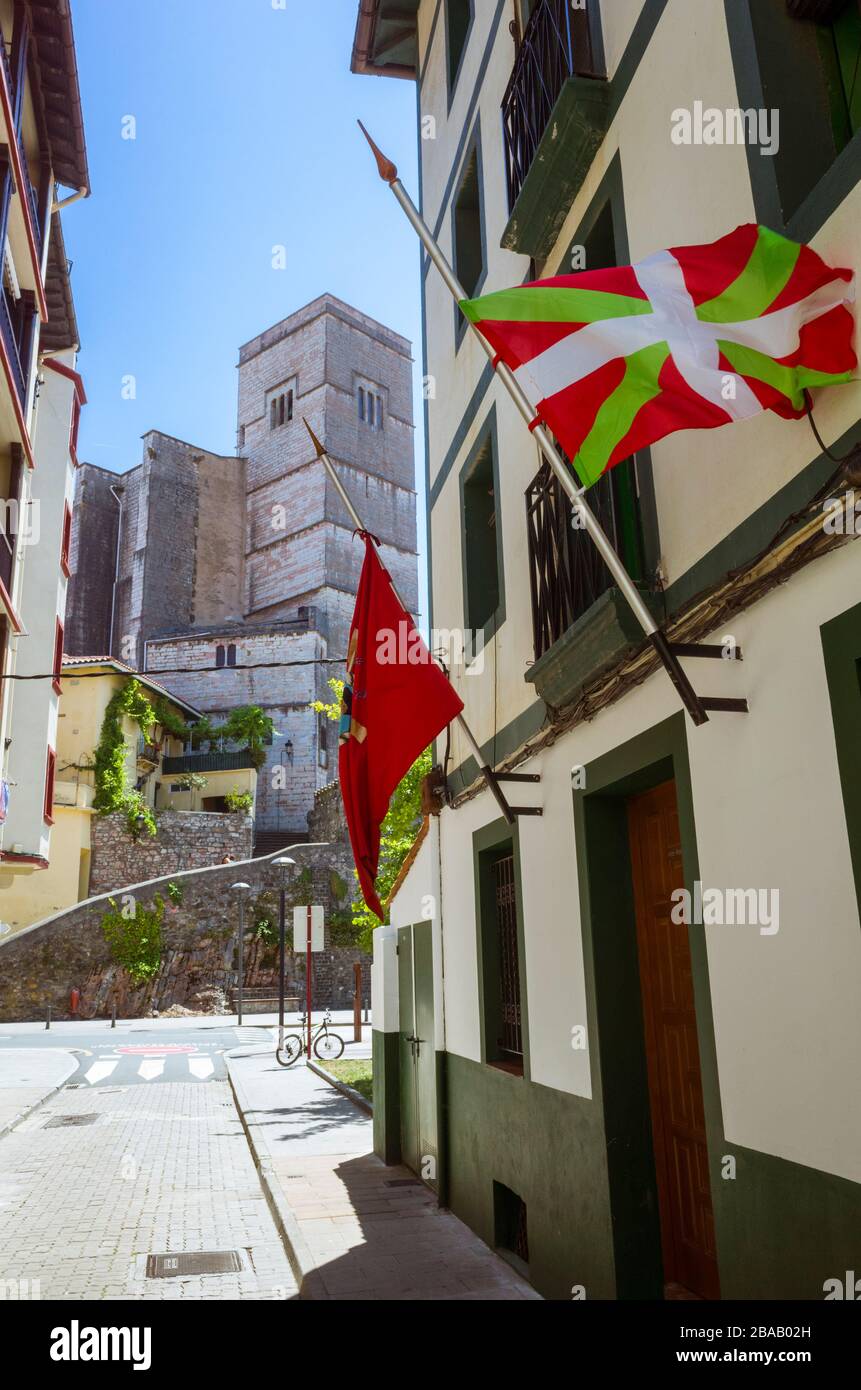 Zumaia, Gipuzkoa, Baskenland, Spanien - 15. Juli 2019 : EINE baskische Ikurrina-Fahne flattert mit der gotischen Kirche San Pedro aus dem 13. Jahrhundert in Backgr Stockfoto
