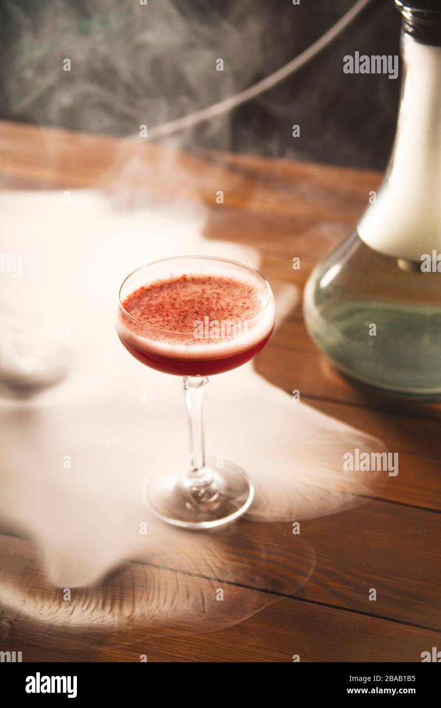 Himbeere alkoholischer Cocktail in einem Glas mit Schaum, mit gefriergetrockneten Himbeeren im Kapuzenrauch auf dem Tisch bestreut. Stockfoto