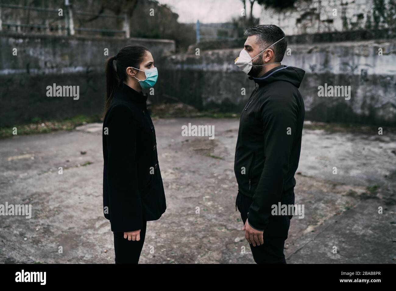 Zwei Menschen in Masken, die aus der Ferne sprechen.Paar, die durch unheilbare Infektionskrankheiten geteilt werden.Infektionskontrolle,Isolation.liebte eine Krankheit.Saying Go Stockfoto