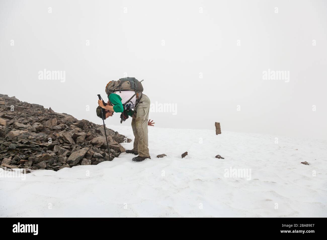 Ein Mann wirft Felsen auf ein Schneefeld, während die Navigation während eines Whiteout auf dem Cooper Mountain, der Kenai-Halbinsel, Alaska, haltet. Stockfoto
