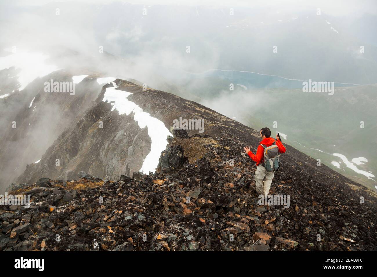 Ein Mann wandert einen Grat durch Wolken unterhalb des Gipfels von Cooper Mountain, Kenai-Halbinsel, Alaska hinunter. Stockfoto
