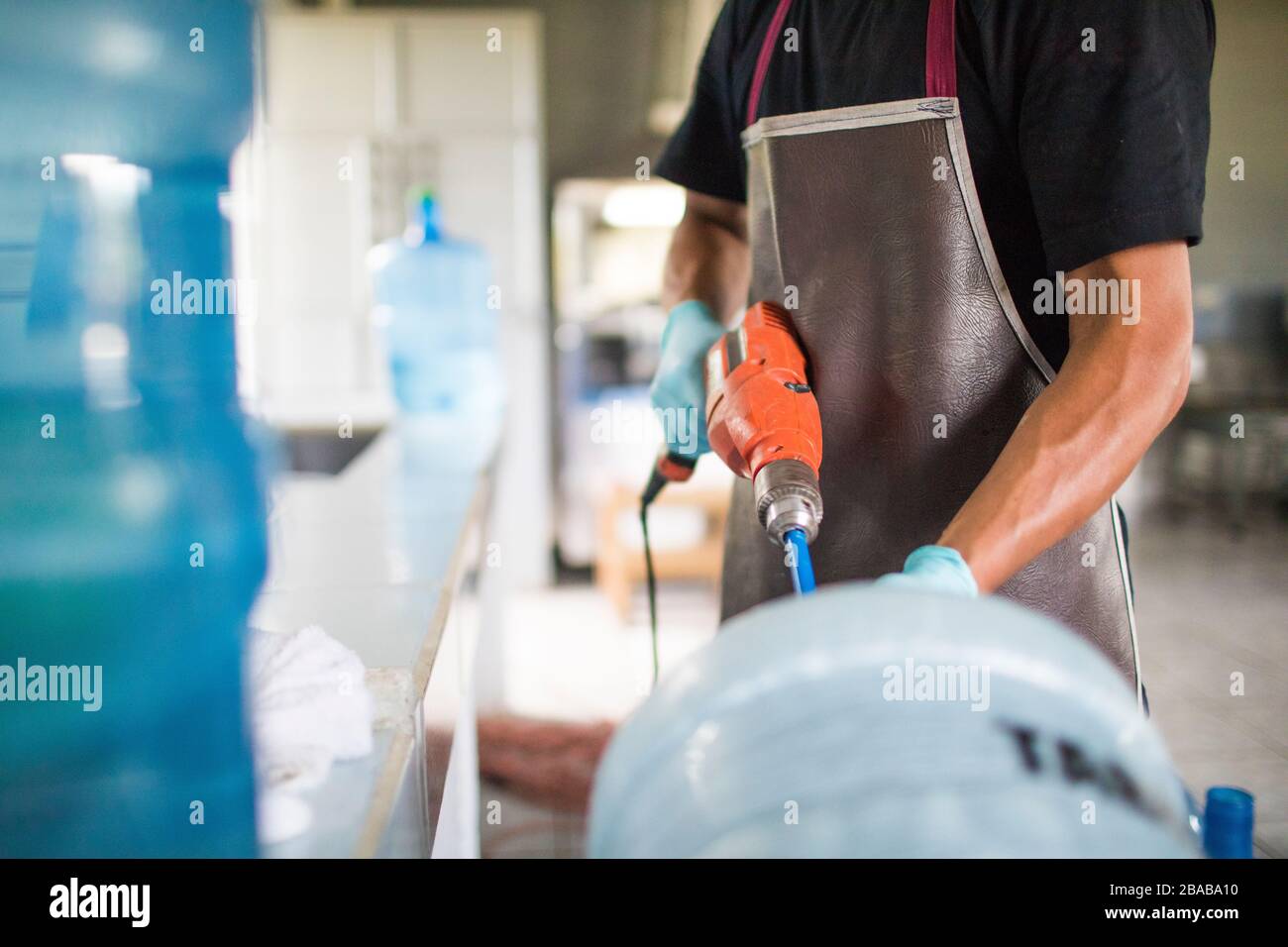 Der Arbeiter spült mit einer Bohrmaschine einen Trinkwasserkrug zur Wiederverwendung aus. Stockfoto