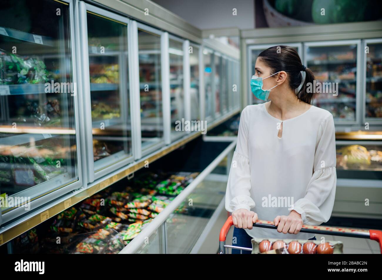 Frau, die Gesichtsmaske trägt, die im Supermarkt kauft.Panic Shopping während Coronavirus Covid-19 Pandemie.Budget Kauf in einem Liefergeschäft.Kauf von Gefriergeräten Smart Stockfoto