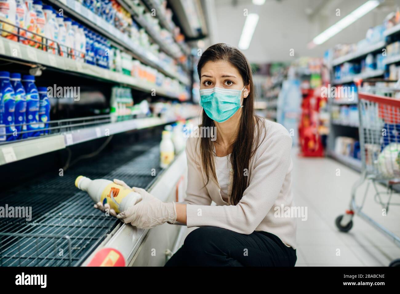 Traurige besorgte Frau, die Gesichtsmaske trägt, die im Supermarkt/Drogerie mit ausverkauftem Zubehör kauft.Leere Regale im Supermarkt wegen neuartigen Coronaves Stockfoto