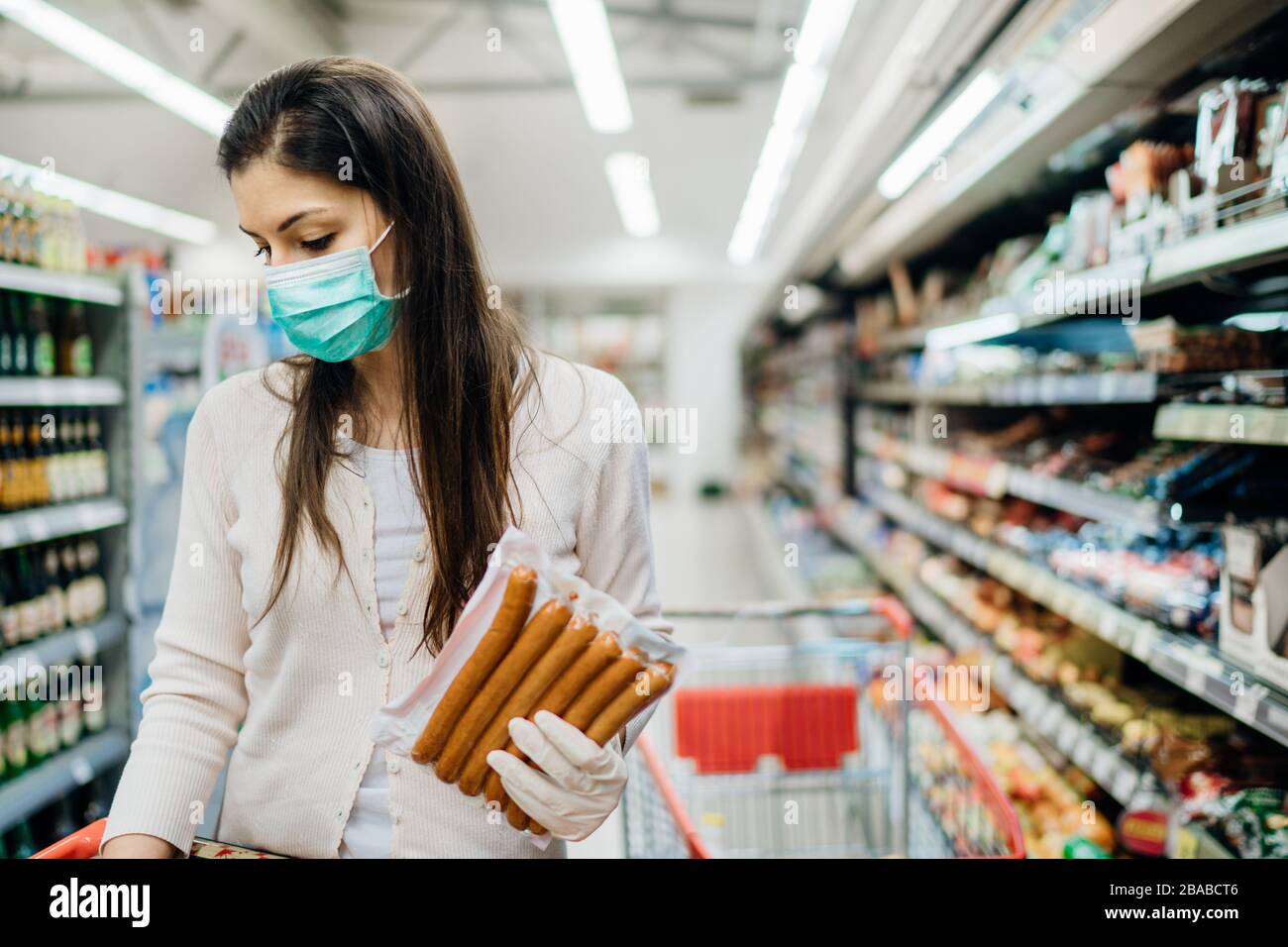 Frau mit Schutzmaske und Handschuhen, die für die Versorgung einkauft.Budget einkaufen in einem Supermarkt.Kauf verarbeiteter, nicht verderblicher Lebensmittel.Vorbereitung für eine pande Stockfoto