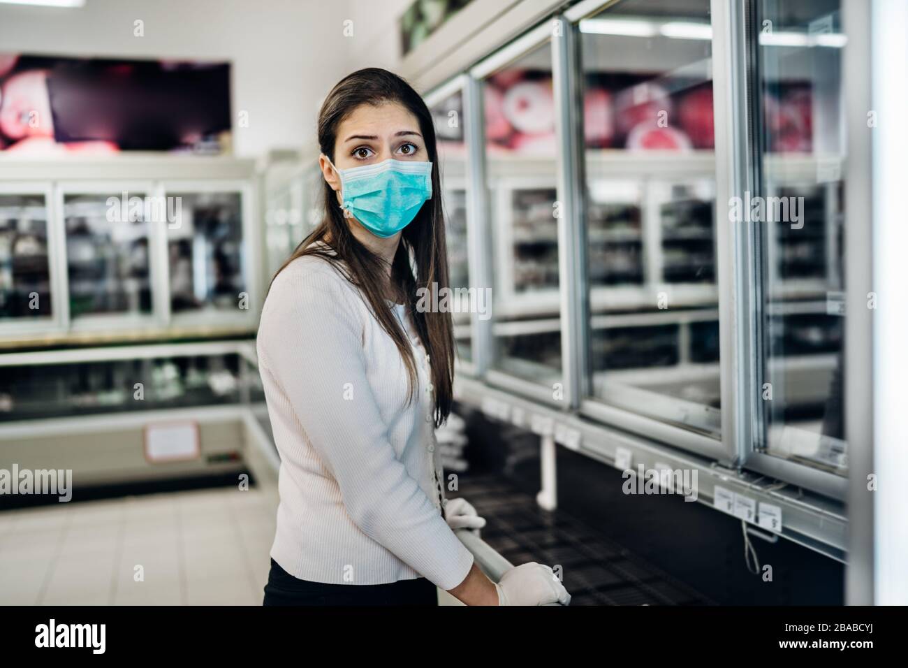 Frau mit Maske und Handschuhen kauft Lebensmittel/Verbrauchsmaterial im Supermarkt mit ausverkauften Produkten.Lebensmittelmangel.Leere Regale wegen neuartiger Korona Stockfoto