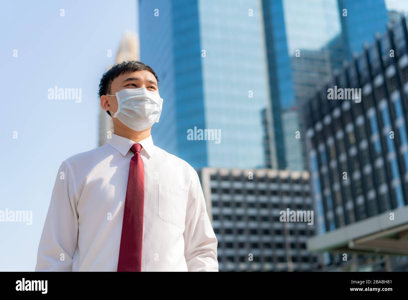 Junger, intelligenter asiatischer Geschäftsmann in weißem Hemd, der in der Verschmutzungsstadt arbeiten wird, trägt er Schutzmaske zur Verhinderung von PM2,5-Staub, Smog, Luftverschmutzung und COVI Stockfoto