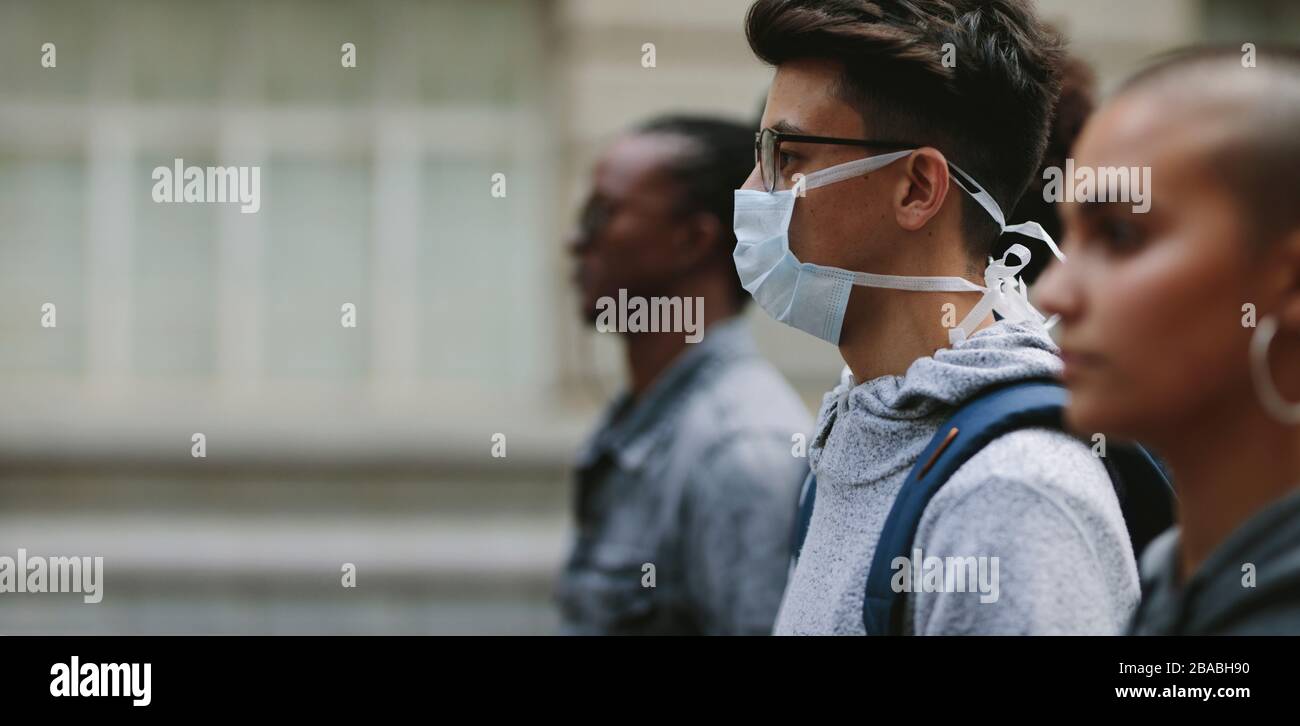 Junger Mann, der eine Maske trägt, die an einem Protest mit Menschen in der Umgebung teilnimmt. Junge Leute auf stille Proteste in der Stadt. Stockfoto