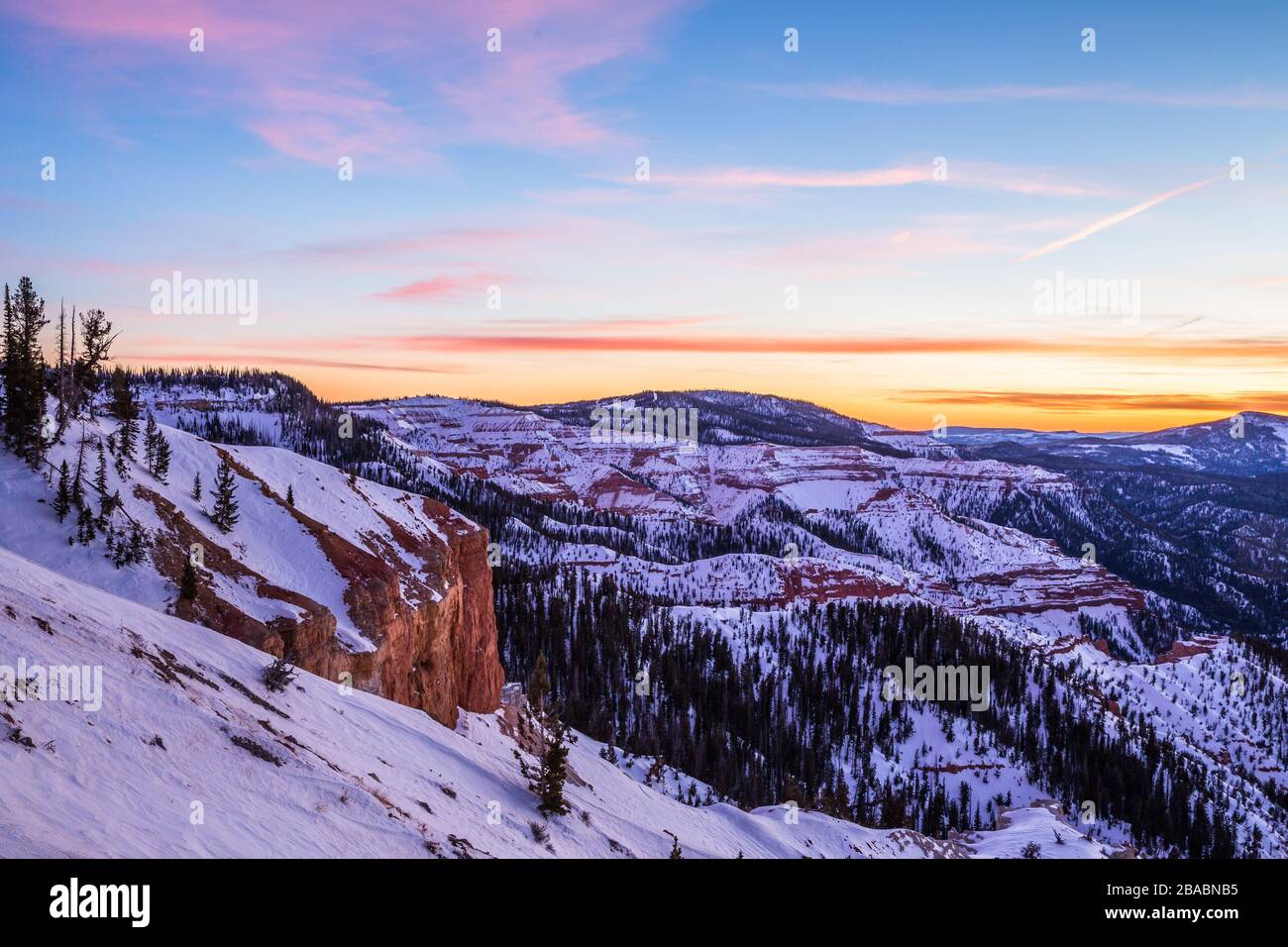 Rosafarbene und orangefarbene Wolken bei Sonnenuntergang über dem Kopf. Darunter orangefarbener und roter Felsen, der in der Winterszene von Southern Utah schneebedeckt ist. Stockfoto