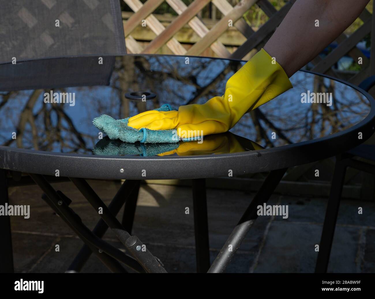 Wischen Sie saubere Gartenmöbel. Die Hand ist mit Gummihandschuhen geschützt. Stockfoto