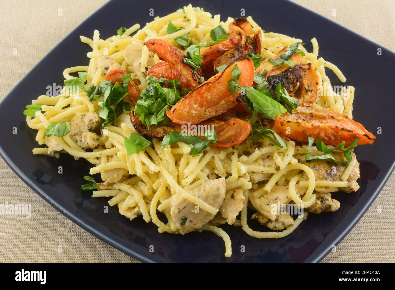 Hähnchenspaghetti mit Basilikum und Tomaten in leichter Sahnesauce auf blauem Teller Stockfoto