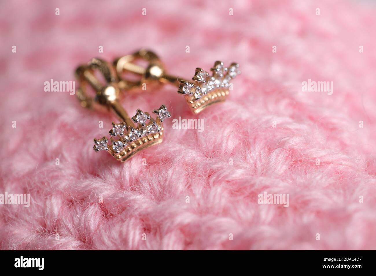 Goldene, kronenförmige Ohrringe auf gestricktem rosafarbenem Stoff. Nahaufnahme. Stockfoto
