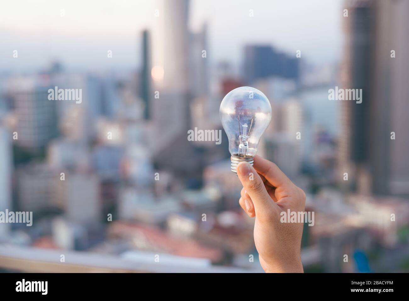 Glühbirne vor Sonnenuntergang städtischen Häuser. Glühlampe transparent Lampe in alternative Solar Energie des Menschen in der Stadt, Stadt, Stadt Nachtleben. Symbol, Konzept der Busi Stockfoto