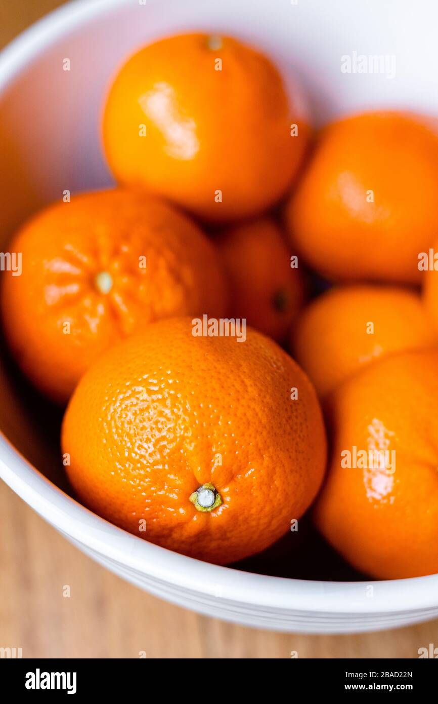 Orangen in einer weißen Schüssel mit Holzhintergrund; köstliche saftige Früchte; Nahmakro mit verschwommem Hintergrund Stockfoto