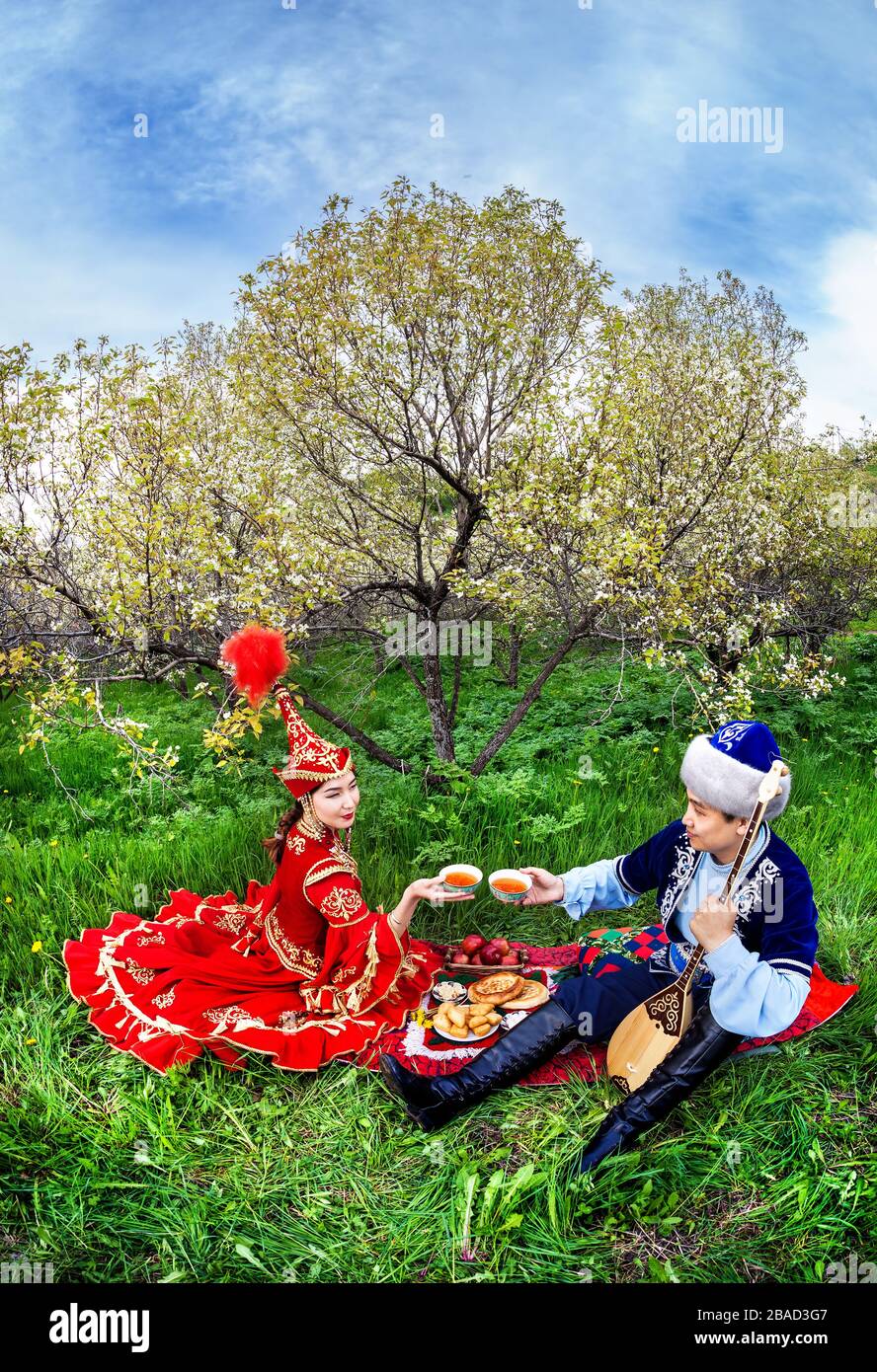 Paar im kasachischen Kostüm sitzen im Frühjahr blühen Apfelgarten bei Picknick in Almaty, Kasachstan, Zentralasien Stockfoto