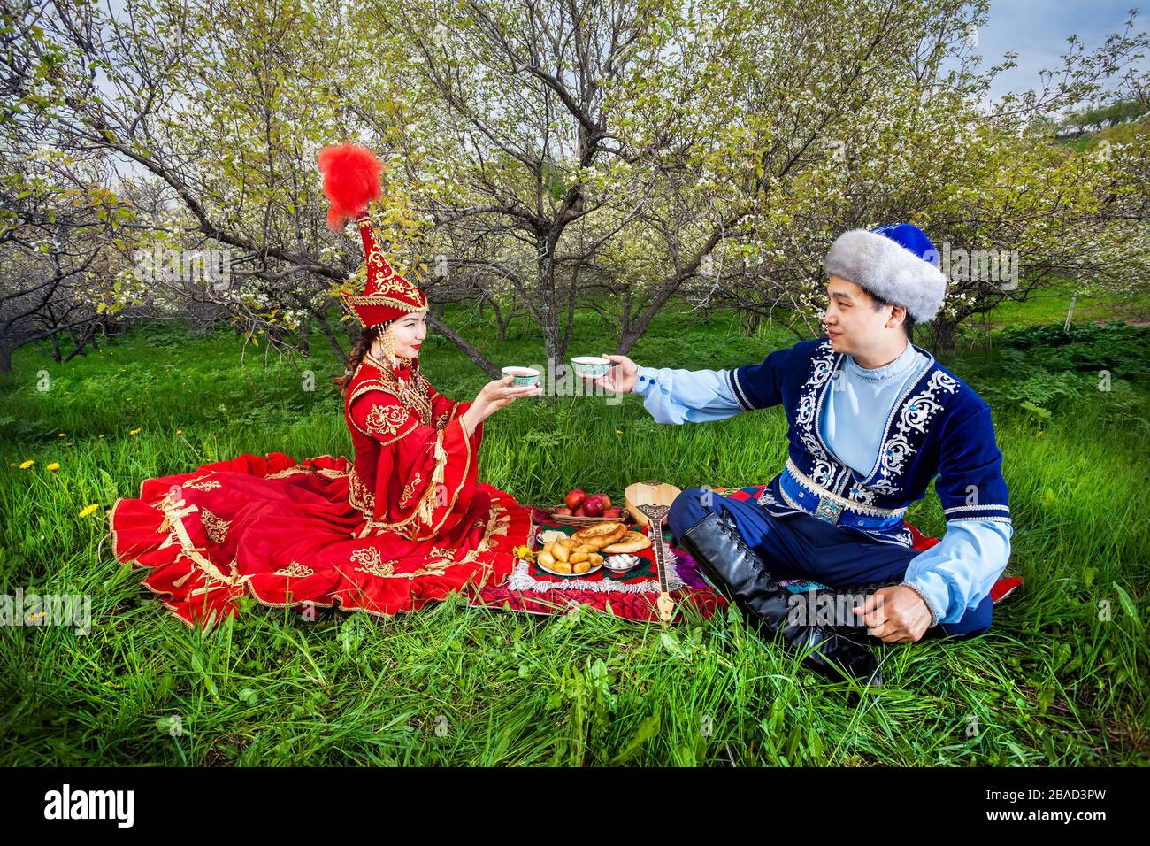 Paar im kasachischen Kostüm sitzt im Frühjahr blühen Apfelgarten bei Picknick und Teetrinken in Almaty, Kasachstan, Zentralasien Stockfoto