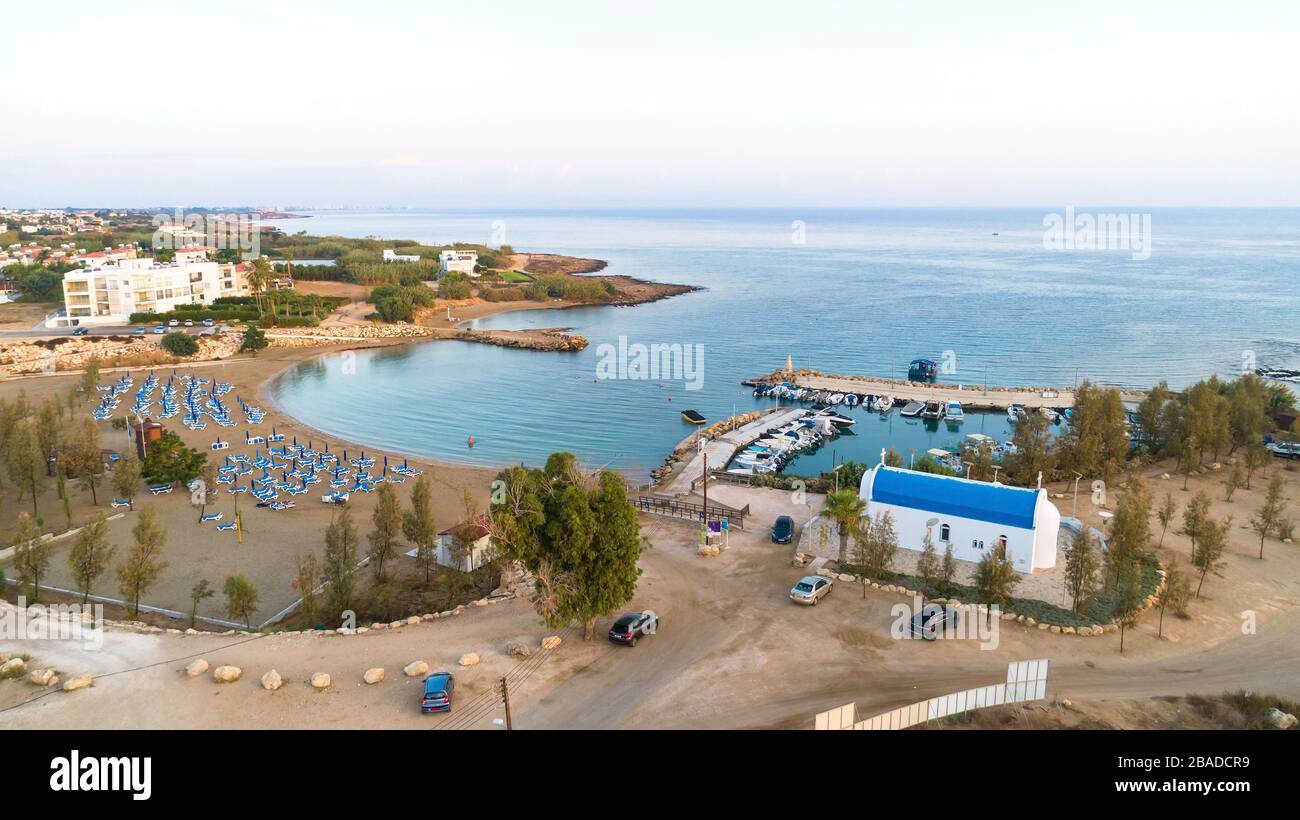 Luftbild des Sonnenuntergangs an der Küste und die weiße, gewaschene Kapelle am Strand Agia Triada, Protaras, Famagusta, Zypern von oben. Vogelperspektive auf Tour Stockfoto
