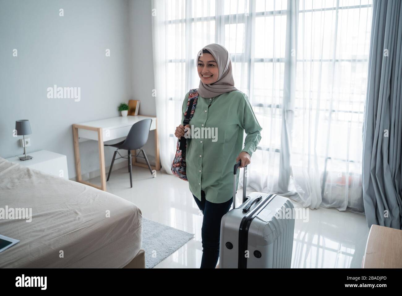 Schöne junge Hijab-Reisende gehen und tragen ihre Tasche und halten Koffer  in den vorderen Fenstern mit Vorhang Stockfotografie - Alamy