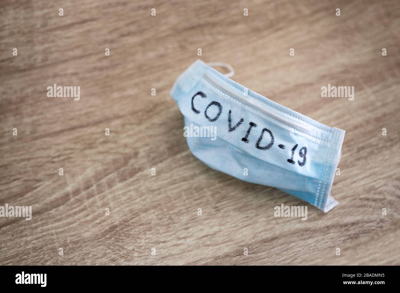 Medizinische Gesichtsmaske mit Text von Covid-19 auf Holztisch Stockfoto