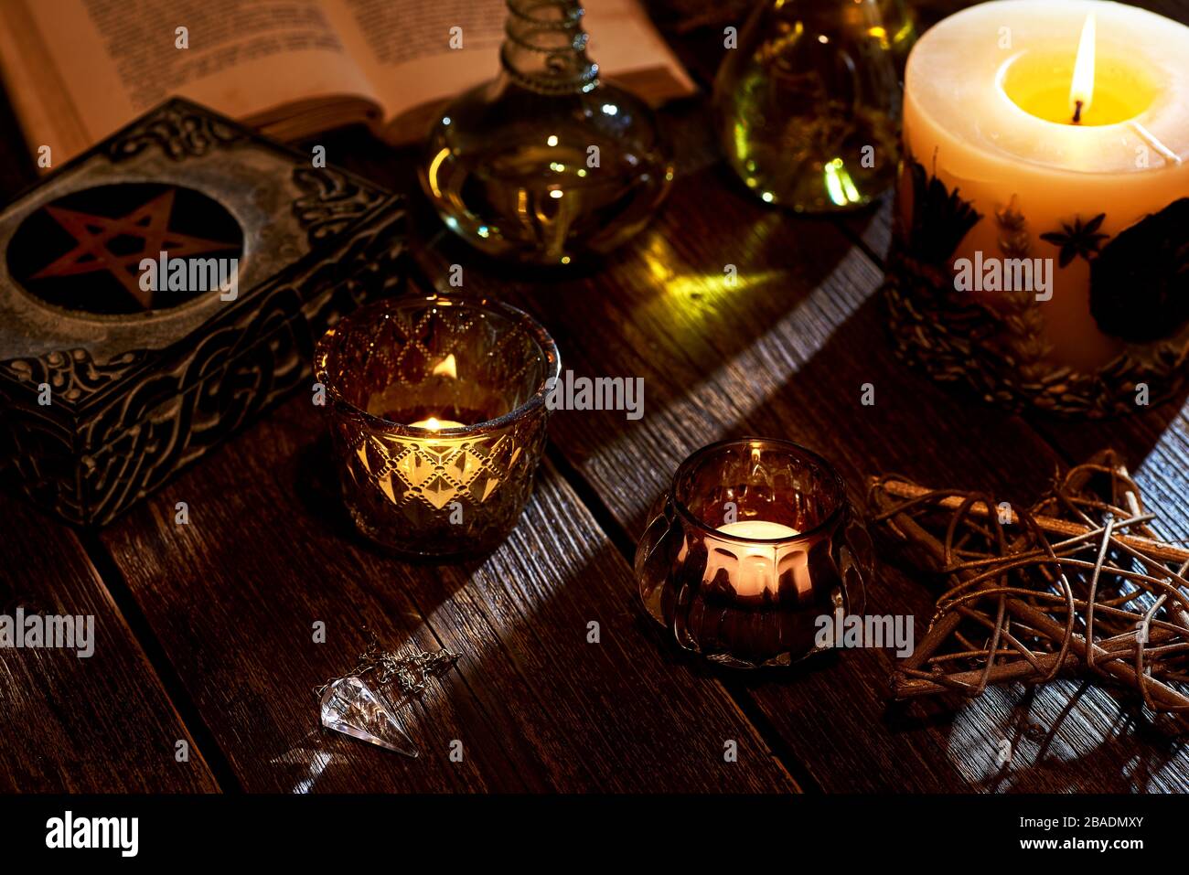Stillleben mit brennender Kerze auf alter Holztischplatte, Zauberbuch und Kiste mit Pentagramm. Geeignet für Magie oder Esoterik. Stockfoto