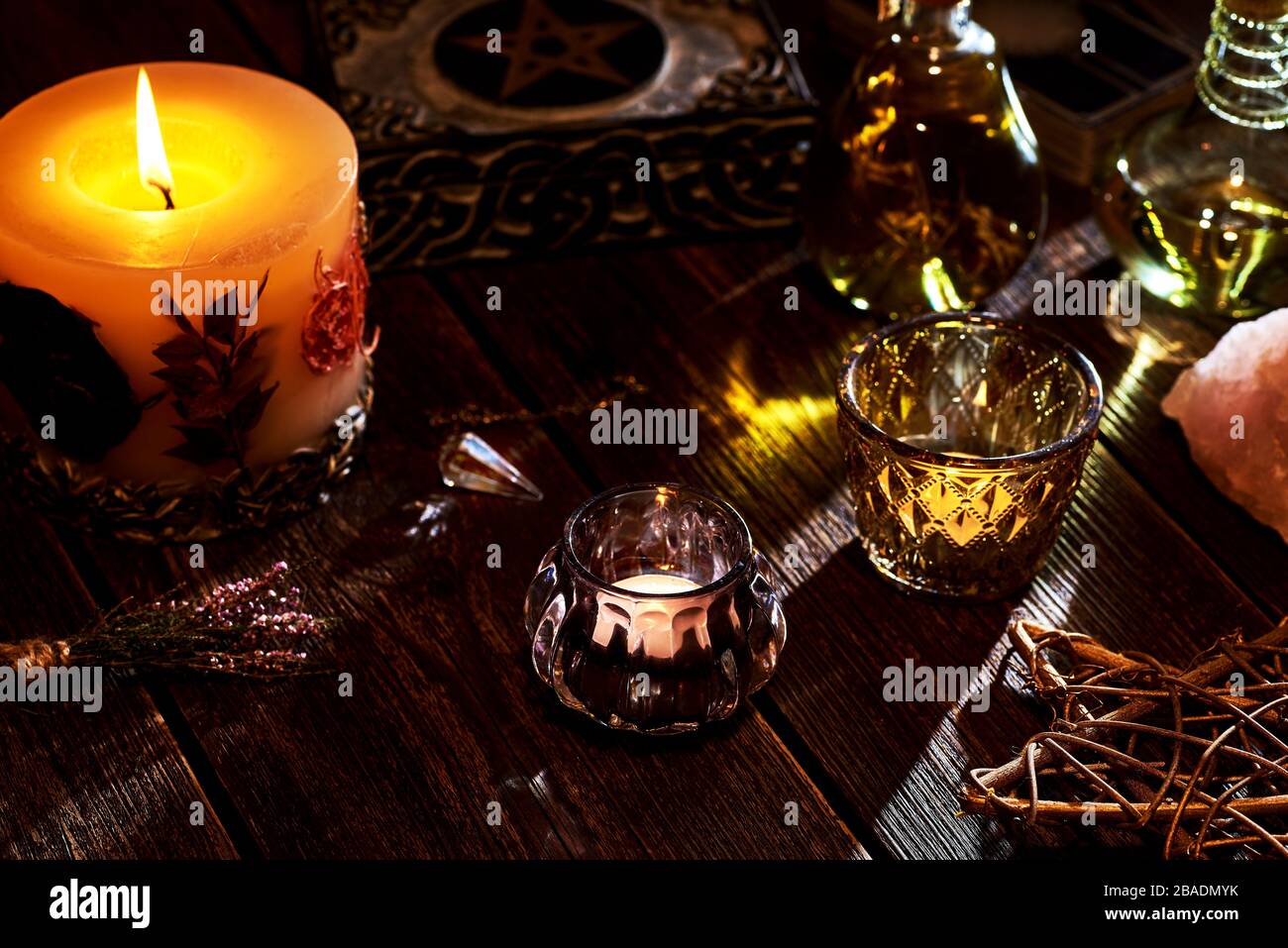 Esoterisches oder mystisches Stillleben mit einer Kiste und ein paar brennenden Kerzen, einem Pentagramm. Pendel und Edelsteine auf alter Holztischplatte. Stockfoto