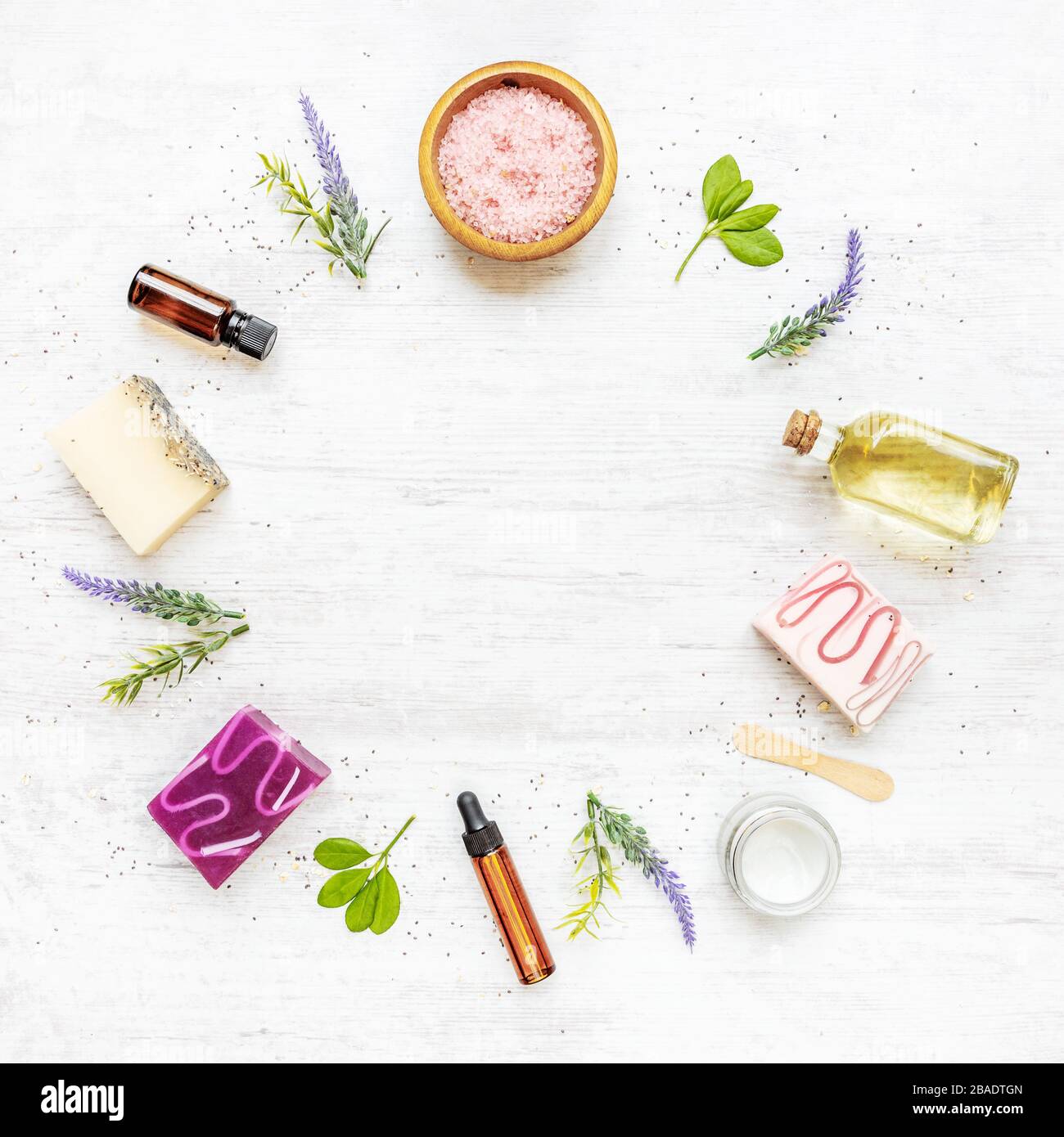 Draufsicht auf organische Seifen und Kosmetik, die im Kreis mit Lavendel, Kräutern, chia und ätherischen Ölen angeordnet sind. Weißer rusrischer Hintergrund, Kopierbereich. Stockfoto