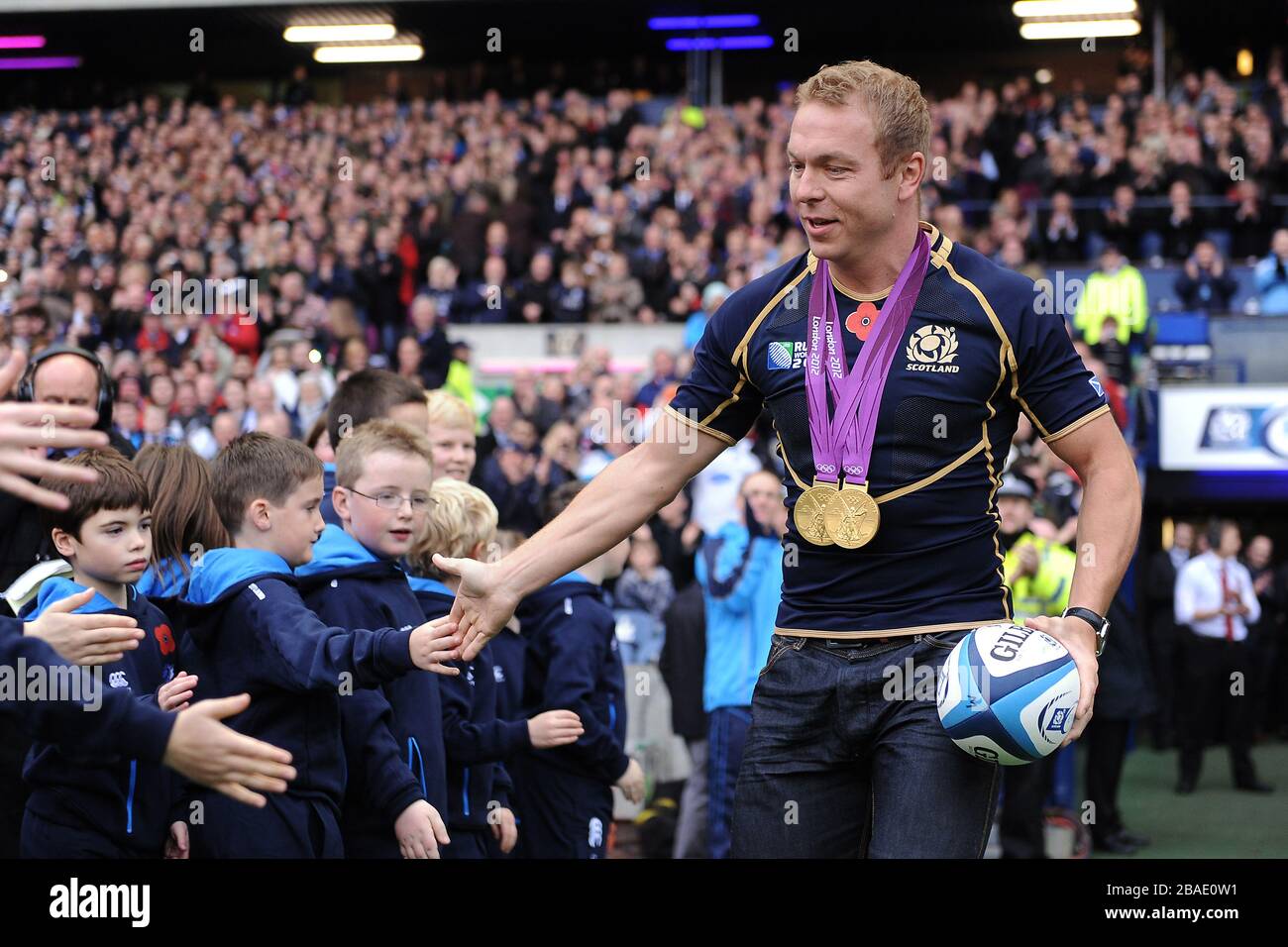 Großbritanniens Olympia-Goldmedaillengewinner Sir Chris Hoy trägt den Spielball auf das Spielfeld Stockfoto