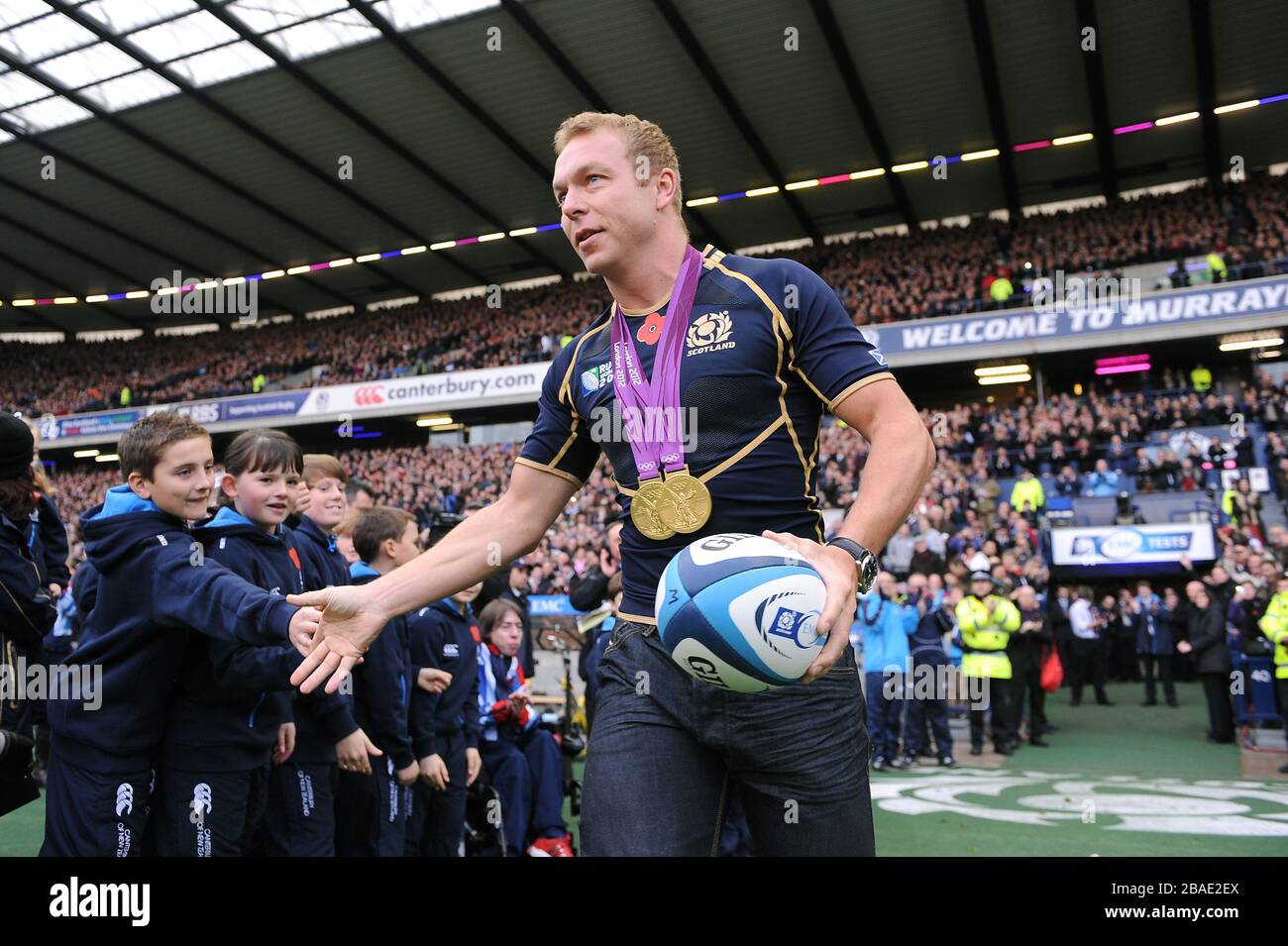 Großbritanniens Olympia-Goldmedaillengewinner Sir Chris Hoy trägt den Spielball auf das Spielfeld Stockfoto