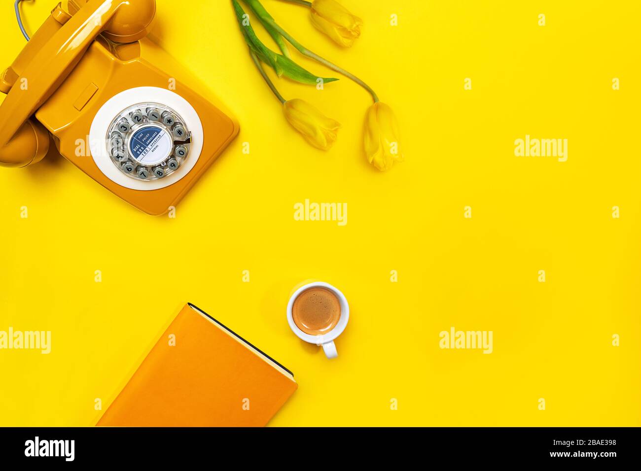 Gelbes Layout mit Retro-Drehtelefon, Tasse Kaffee, Blumen und Notizbuch. Flaches Layout, Draufsicht, Kopierbereich. Stockfoto