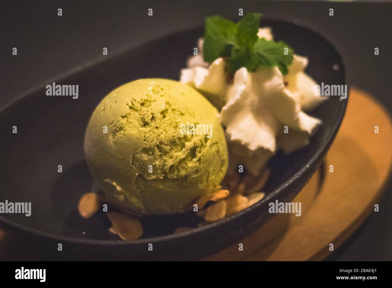 Ein Ball aus matchgrünem Teeeis und Mandelflocken sowie Schlagsahne und Minzblättern Stockfoto