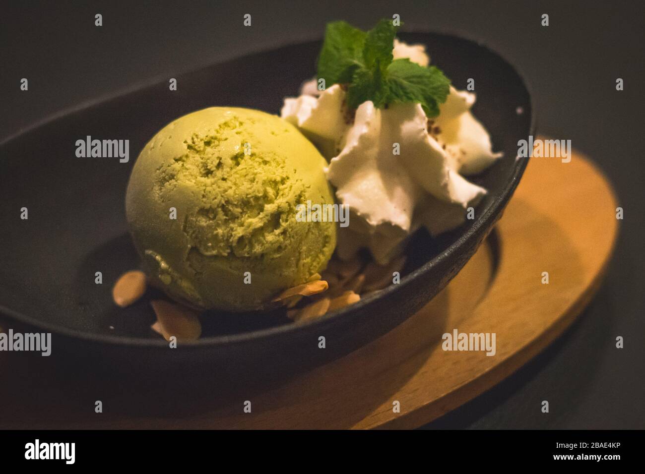 Ein Ball aus matchgrünem Teeeis und Mandelflocken sowie Schlagsahne und Minzblättern Stockfoto