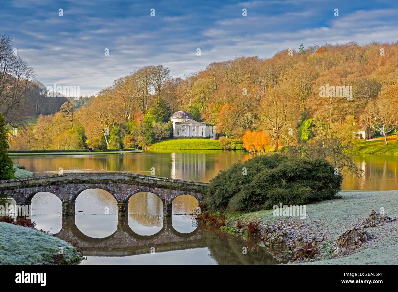 Am frühen Morgen erleuchten Frost und strahlender Wintersonne einige der Bäume, die den See umgeben, in Stourhead Gardens, Wiltshire, England, Großbritannien Stockfoto