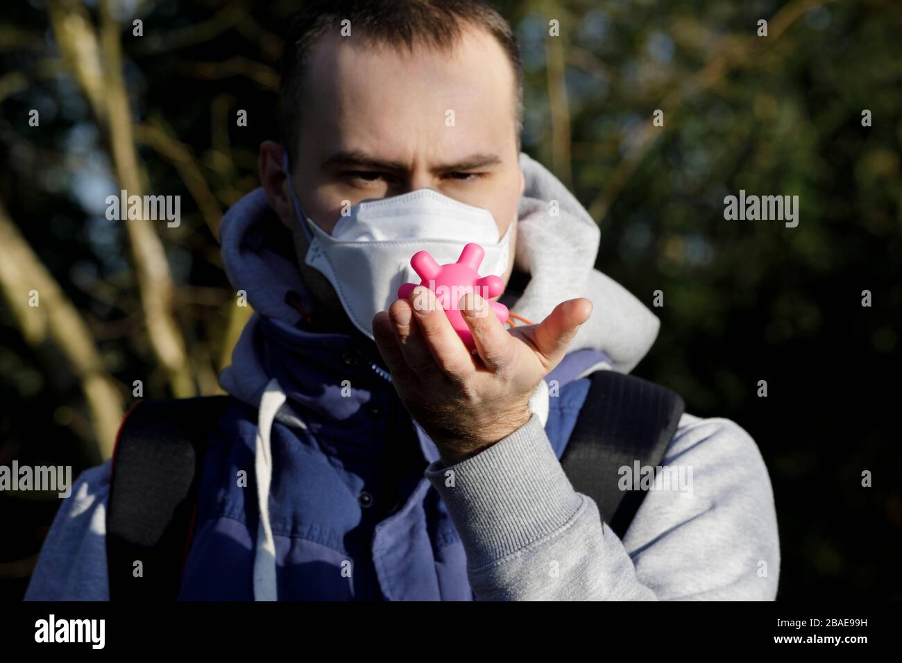 Junger Erwachsener, der eine Verschmutzungsmaske trägt, um sich vor Corona-Viren Covid-19 zu schützen. Corona-Virus-Konzept. Der Junge hält ein kovid-19-Virus an der Hand Stockfoto